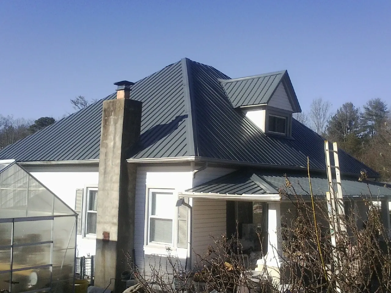 Dark blue standing seam metal roof on a white farmhouse with dormer — Slate & Tile Roof Repair by Roofing Brothers in Hustle