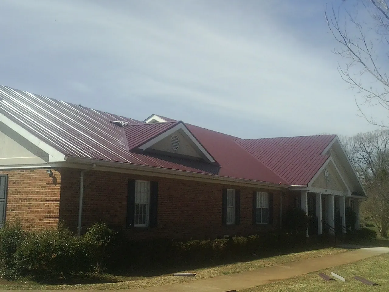 Red metal roof with gabled entries on a long brick building, from a Hail Damage Roof Repair job in Hustle