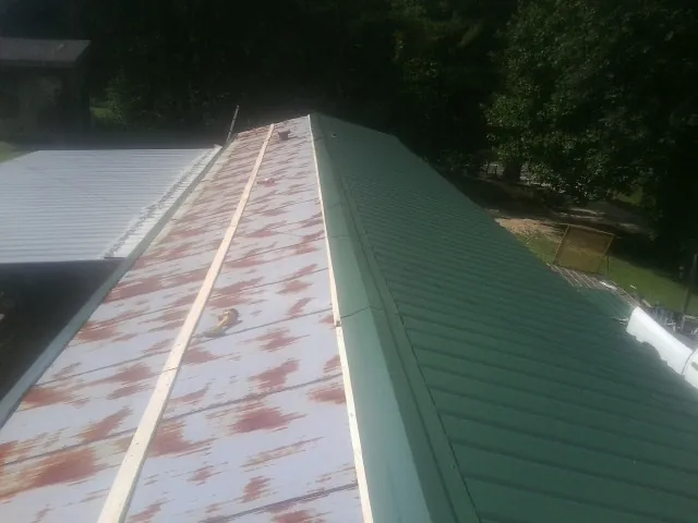 Old rusted panels beside newly installed green metal roofing — Wind Damage Roof Repair by Roofing Brothers in Hustle