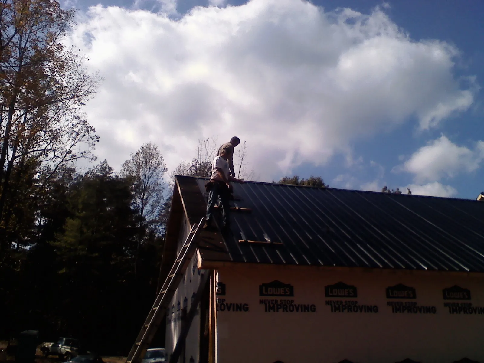 Roofer fastening dark metal panels high against a cloudy sky, from a Roof Inspection job in Hustle