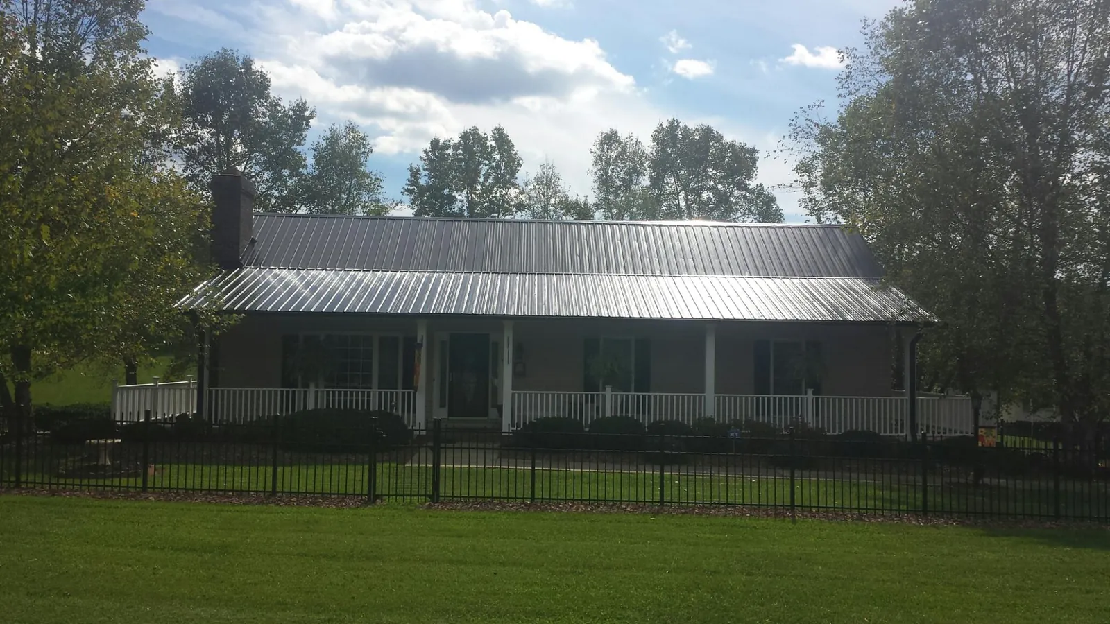 Gray metal roof on a brick ranch with a full width front porch — Gutter Guard Installation work by our crew in Hustle