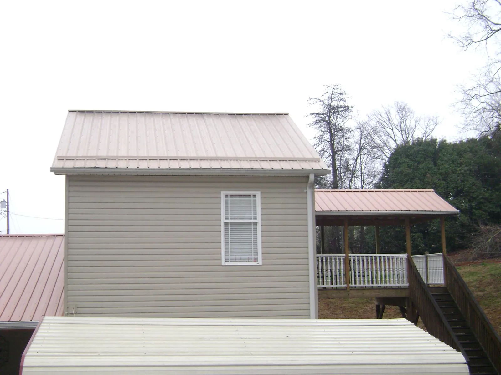 Tan metal roofs on a two story addition and attached porch, from a Roof Replacement job in Hustle